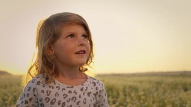 Sahadaki küçük kız. Çocuk ayağa kalkar ve gökyüzüne bakar. Sonra kafasını çevirir. Uzun kıvırcık saçlı güzel kız..