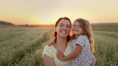 Anne, kızını kollarında tutuyordu. Arazinin ortasındalar. İkisi de gülümsüyor..
