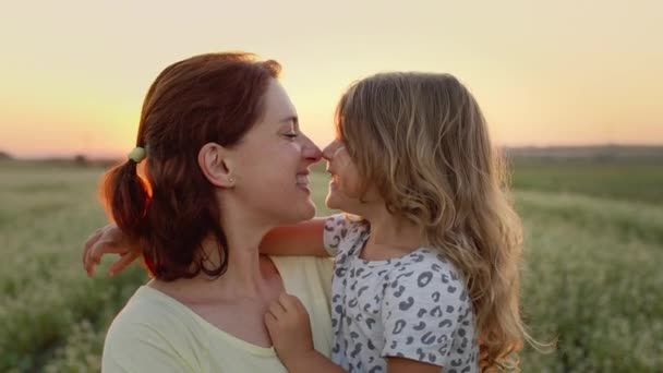 Die junge Mutter hält ihre Tochter im Arm. Sie befinden sich in der Mitte des Feldes. Beide lächeln. Mädchen berührt ihre Mutter Nase mit der Nase. — Stockvideo