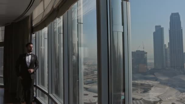 Joven hombre con estilo en traje camina a lo largo de la ventana grande. Desde La Ventana Vista De Dubai Desde Altura. — Vídeo de stock