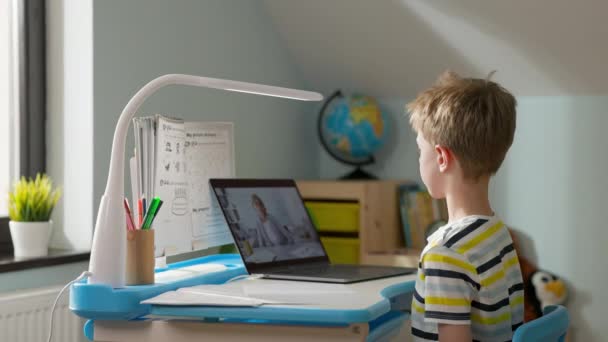 Junge sitzt zu Hause am Laptop. Online-Lektion. Kind grüßt den Lehrer. Fernstudium. — Stockvideo