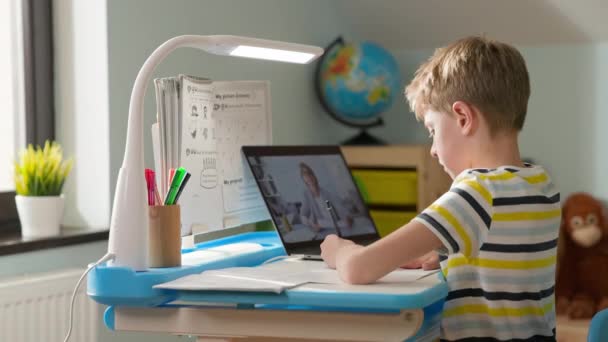 De jongen zit thuis op Laptop. Online les geven. Jongen steekt zijn hand op. Hij wil vragen beantwoorden tijdens de les.. — Stockvideo