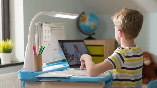 Chłopiec siedzi na laptopie w domu. Lekcja online. Dziecko uważnie słucha nauczyciela patrzącego na ekran laptopa. — Wideo stockowe
