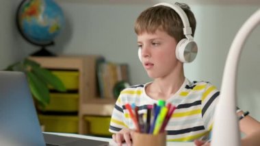 Yedi Yaş Çocuğu. Dizüstü bilgisayara bakan çocuk. Kulaklıklarını mutsuz bir şekilde çıkarıyor ve elini masaya vuruyor. Çok kızgın..