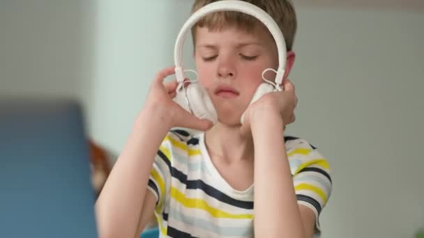Hétéves fiú arca. Nézi a fülhallgatóját. Ideges és leveszi a fejhallgatóját.. — Stock videók