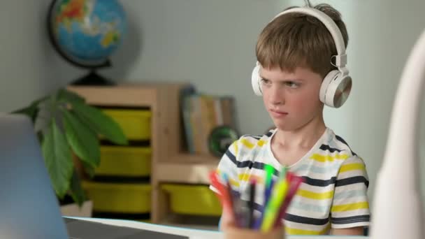 Garçon de sept ans. Garçon regardant l'écran d'ordinateur portable. Il enlève ses écouteurs malheureux et tape sa main sur la table. — Video