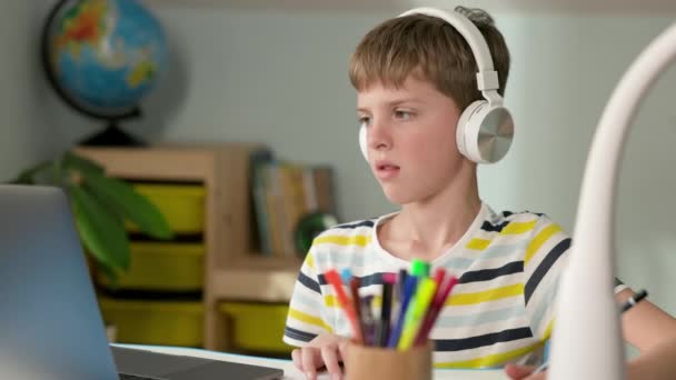 Junge von sieben Jahren. Junge schaut auf Laptop-Bildschirm. Unglücklicherweise nimmt er seine Kopfhörer ab und tippt mit der Hand auf den Tisch. Er ist wütend. — Stockvideo