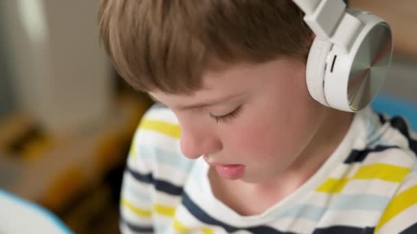 Egy hétéves fiú arca fülhallgatóban. Aranyos szőke fiú.. — Stock videók