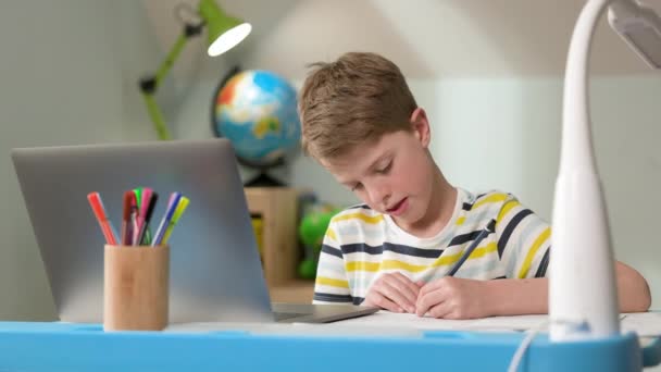 Niño sentado en el portátil en casa. Lindo niño de siete años dibuja. — Vídeos de Stock