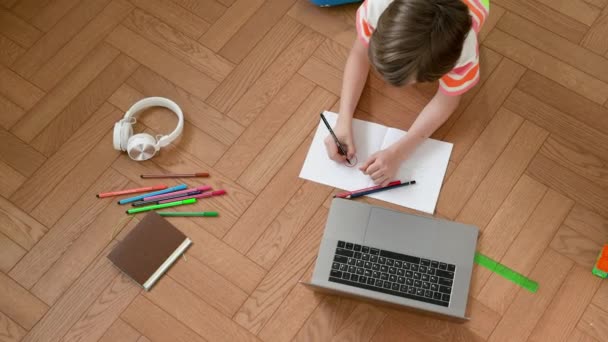 Fiú feküdt a padlón Laptop előtt. Jegyzetfüzetbe ír.. — Stock videók