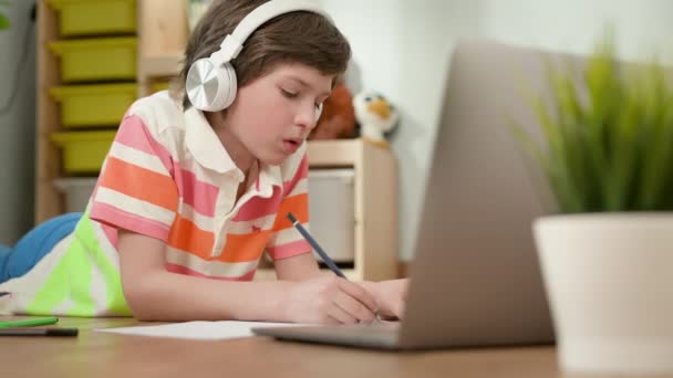 男孩躺在笔记本电脑前的地板上。他写在笔记本上. — 图库视频影像