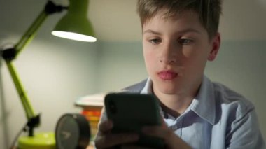 On yaşında bir çocuk elinde telefonuyla odasında oturuyordu. Kulaklıklar kafasında. Oda lambayla aydınlatıldı..