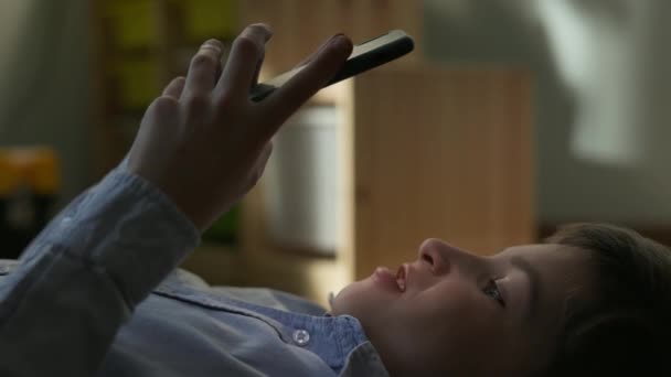 Ragazzo di dieci anni sdraiato con il telefono in mano. Lui è molto felice. — Video Stock