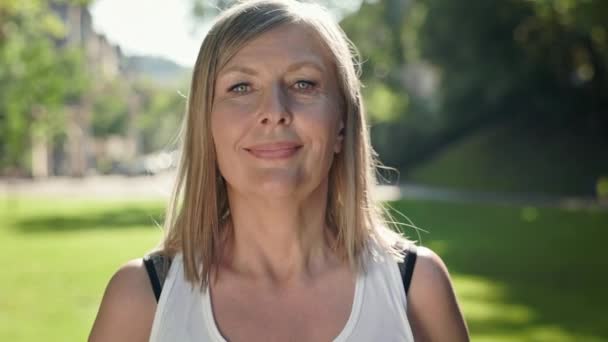 Verouderde vrouw gaat sporten in het park. Ze heft haar armen op met duimbellen en haalt diep adem.. — Stockvideo