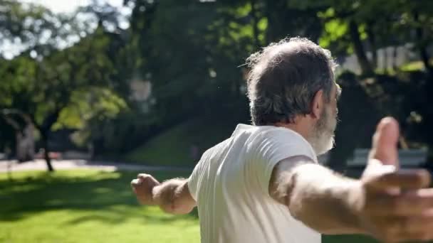 Oude man gaat sporten in het park. Hij doet aan armoefeningen. grijze harige man met baard. — Stockvideo