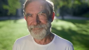Sakallı, gri saçlı adamın yüzü. O, parkta. Gülümsüyor..