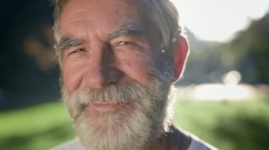 Sakallı, gri saçlı adamın yüzü. O, parkta. Gülümsüyor..