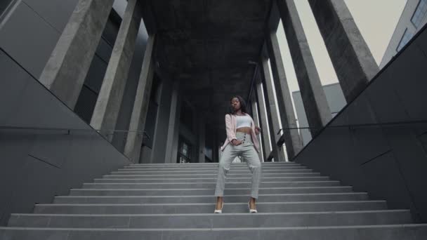 Το κορίτσι κατεβαίνει τις σκάλες. Νεαρή μαύρη κοπέλα που χορεύει μοντέρνο χορό στις σκάλες. Φοράει επαγγελματικά ρούχα με ψηλά τακούνια.. — Αρχείο Βίντεο