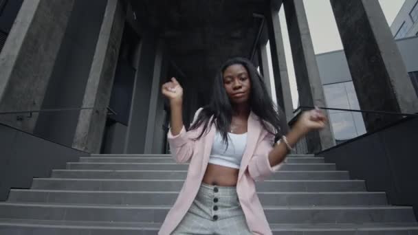 Zwart meisje danst moderne dans op de trappen. Ze draagt zakelijke kleren. Dan nadert de camera het meisje en gaat dan weg. Haar maag is kaal.. — Stockvideo