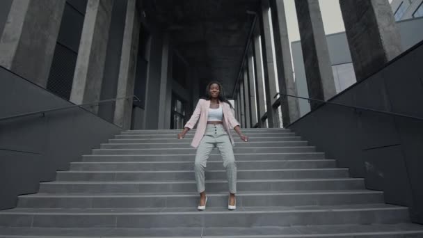 Молодая чёрная девушка танцует современный танец на лестнице. Она в деловой одежде на высоких каблуках. Она танцует, а потом останавливается. — стоковое видео