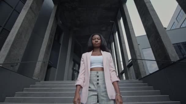 Joven chica negra de pie en las escaleras del edificio. Ella está elegantemente vestida con estilo de negocios. — Vídeo de stock