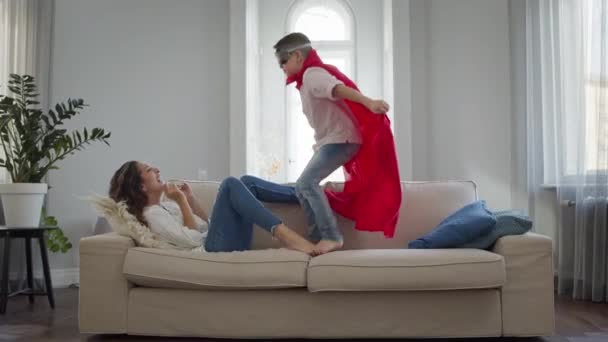 Máma a syn v pokoji. Chlapec v červeném plášti a brýle hraje. — Stock video