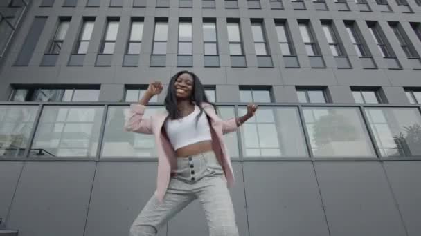 Hermosa chica negra bailando en la calle. Detrás de sus altos edificios. Bailes modernos. Ella levanta su pierna alta. — Vídeo de stock