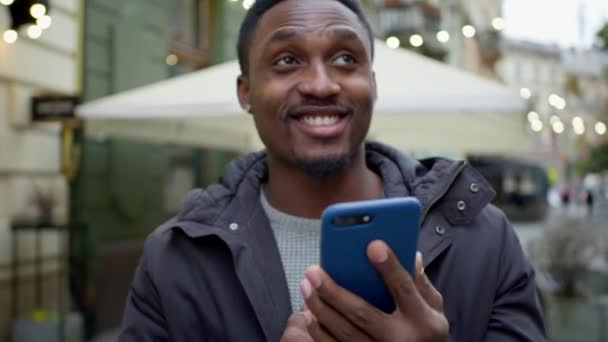 Genç siyahi adam elinde telefonla caddede yürüyor. Telefonu sanki biriyle mektuplaşıyormuş gibi kullanıyor.. — Stok video