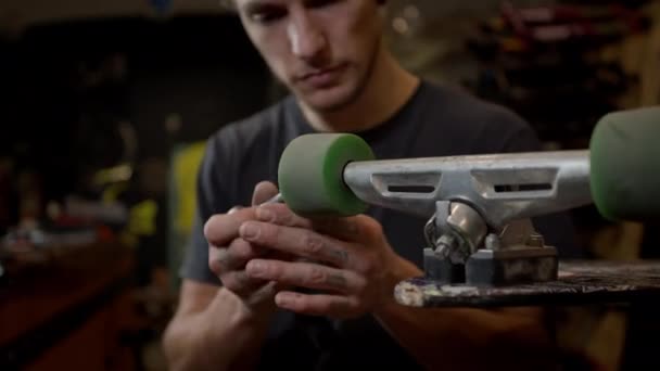 Young Man In The Workshop Attaches Wheel To Skateboard. Many Tools And Parts In The Workshop. Handsome Guy With Beard Works Carefully. Close Up. — Stock Video