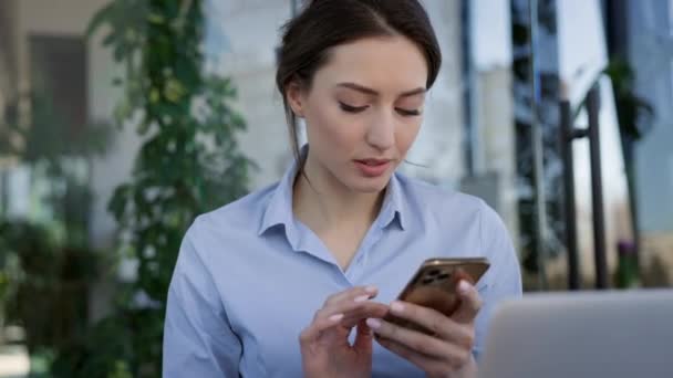 Młoda dziewczyna pracuje w biurze. Siedzi przy stole i trzyma telefon komórkowy w rękach.. — Wideo stockowe