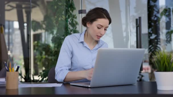 사무실에서 일하는 소녀. 노트북 과 일하는 곳 에 앉아 있는 예쁜 브루넷이야. 그녀는 문서를 가지고 일한다. — 비디오