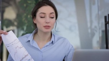 Ofisteki Genç Esmer 'in Portresi. Laptop monitörünün önünde otururken aktif olarak bir şeyler anlatıyor. Dizüstü bilgisayardaki birine bir kağıt parçası gösteriyor..