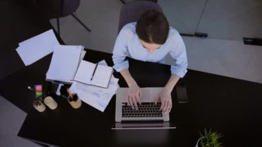 Ofisteki genç esmer. Dizüstü bilgisayar monitörünün önünde oturuyor. Üst Manzara. Kız Klavye Tuşlarına Basıyor.