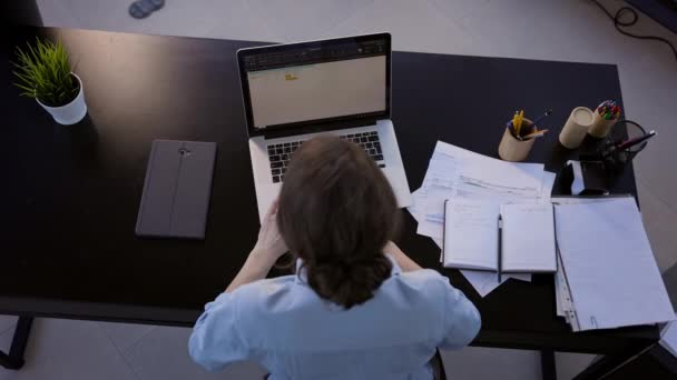 Jung brünette im die büro. Sie sitzt vor dem Laptop-Monitor. Draufsicht. Girle drückt die Tasten der Tastatur. Mädchen hebt ihre Hände nach oben und dehnt sich. — Stockvideo