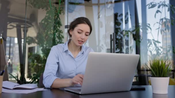 Joven morena en la oficina. Ella está sentada frente al monitor del ordenador portátil. Vista superior. Girle presiona las teclas del teclado. Ella levanta sus manos y se estira. — Vídeos de Stock