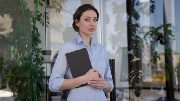 Młoda pracownica biurowa stoi z notatnikiem w rękach. Dziewczyna uśmiechnięta. — Wideo stockowe