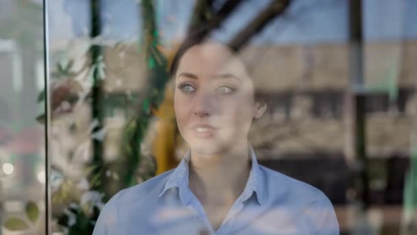 Fille debout dans le bureau. Employé de bureau. Elle se tient derrière la porte transparente. Dans le verre de sa réflexion. — Video