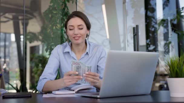 Jeune fille employée de bureau assise à la table. Elle embrasse l'argent et le tient près d'elle. Fille souriante. — Video