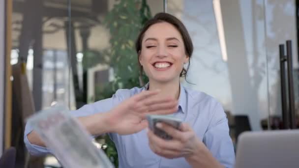 Jeune fille employée de bureau assise à la table. Elle compte l'argent et sourit. Répandre tout l'argent qu'elle lève les mains. Fille heureuse. — Video