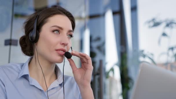 Het gezicht van een jong meisje. Ze heeft een koptelefoon en een microfoon. Ze is aan het praten. Medewerker van het call center. — Stockvideo