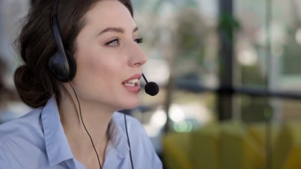 Tvář mladé dívky. Je ve sluchátkách a s mikrofonem. Ona mluví. Zaměstnanec call centra. — Stock video