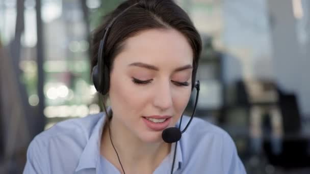 Het gezicht van een jong meisje. Ze heeft een koptelefoon en een microfoon. Ze is aan het praten. Medewerker van het call center. — Stockvideo