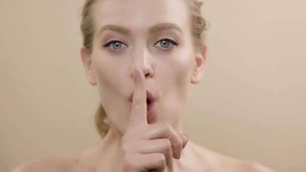 Gezicht van stijlvol jong model met mooie huid. Meisje houdt vinger aan haar mond alsof ze zwijgt. Ze beweegt haar ogen in verschillende richtingen.. — Stockvideo