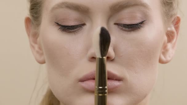 Tvář dívky se zavřenýma očima. Blondýny drží make-up štětec v přední části obličeje. — Stock video