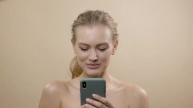 Güzel ciltli şık genç bir manken. Stüdyoda elinde telefonuyla sarışın. Gülümsüyor.