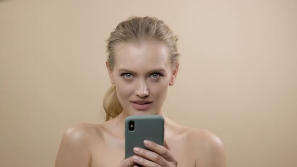 Stylový mladý model s krásnou pletí. Blondýnka ve studiu s telefonem v ruce. She Smiles. — Stock video