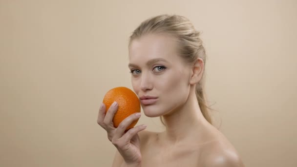 Модель в студії позування. Молода блондинка з довгим волоссям тримає апельсин . — стокове відео