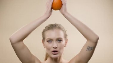 Model In Studio Poz. Uzun saçlı, portakal tutan genç bir sarışın. Kafasında iki eliyle bir portakal tutuyor..