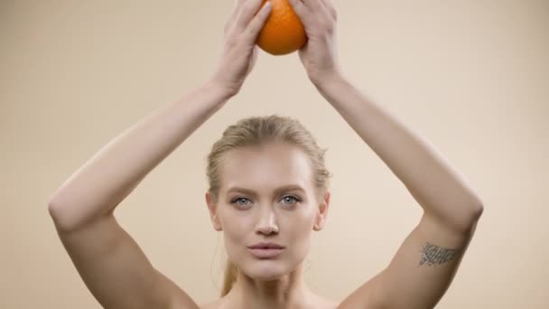 Model di Studio Posing. Blonde Muda Dengan Rambut Panjang Memegang Jeruk. She Holds An Orange Over Her Head With Both Hands. — Stok Video