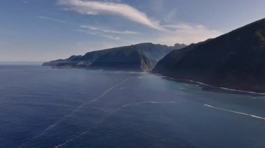 Yukarıdan yemyeşil burunları olan sakin mavi sular, yumuşak dalgalar ve kayalık kıyı şeridinde parlak sabah güneşi.